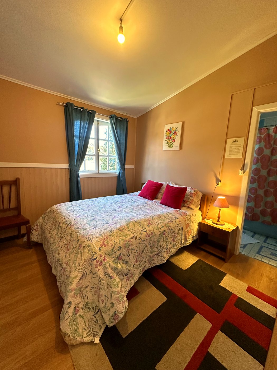 Habitación 1: cama matrimonial con cubrecama floral, cojines rojos y cortinas turquesa, en la casa histórica Von Bischoffshausen