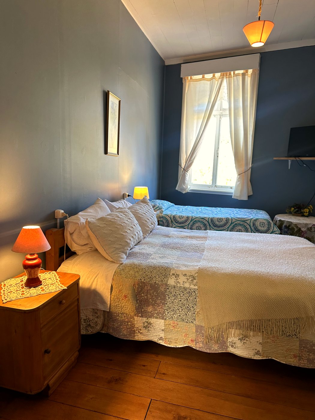 Habitación 3: cama matrimonial junto a pared azul petróleo, con cuadro floral y puerta hacia el pasillo