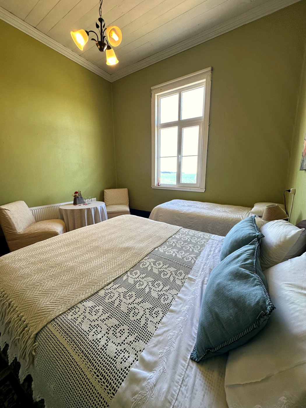 Habitación 5: cama matrimonial y cama adicional en tonos verde oliva, con rincón de estar y vista al lago