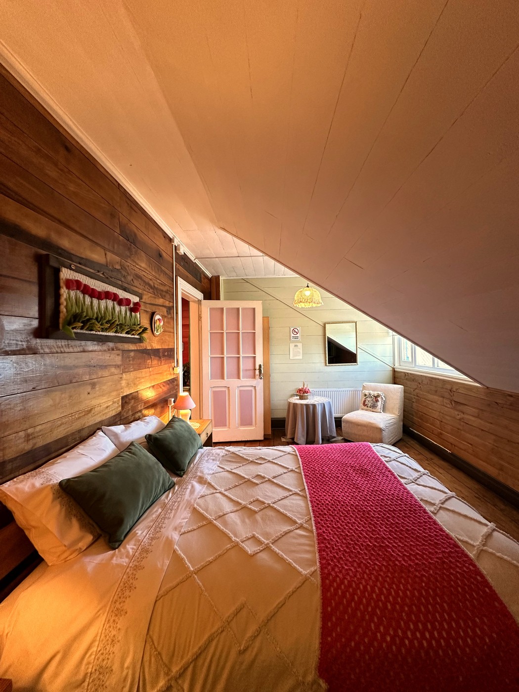 Habitación 6: buhardilla con cama matrimonial vestida en blanco y manta artesanal roja, con vista al lago